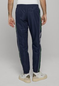 Námořnické teplákové kalhoty se zelenými pruhy po stranách a bílým lemem. Mají elastický pas a manžety u kotníků. Součástí je zadní kapsa.