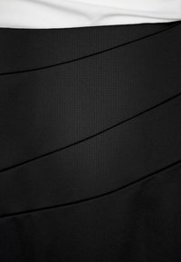 Svart strukturerad tyg med diagonala paneler. Slät textur, med en ren, minimalistisk design. Vit topp är delvis synlig ovanför.