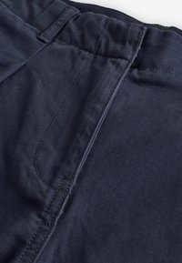 Pantaloni in cotone blu navy con una superficie liscia, dotati di una vita piatta, passanti per la cintura e una cucitura a contrasto lungo le cuciture.
