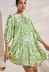 Rochie verde cu un model în culori, cu mâneci bufante, decolteu în formă de inimă și tiv cu volane. Țesătura are un design abstract cu stropi.