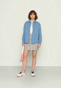 Camisa de ganga azul clara, top branco cropped, saia mini xadrez e ténis rosa com pormenores pretos. Acessórios incluem uma mala rosa.
