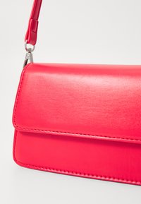Rode leren handtas met een gladde textuur, rechthoekige vorm en klep-sluiting. Bevat zilverkleurige hardware en een afneembare schouderband.