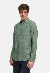 Camicia di lino verde con colletto, maniche lunghe e bottoni in legno; presenta una sottile texture e un piccolo logo sul petto.