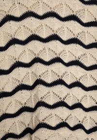 Tessuto lavorato a maglia con sfondo crema e strisce zigzag nere alternate. Design aperto e testurizzato con motivi simili a foglie.