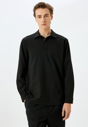 Camisa polo negra de manga larga con collar plano, tapeta de tres botones y dobladillo recto. Tejido suave y ligero con un corte relajado.