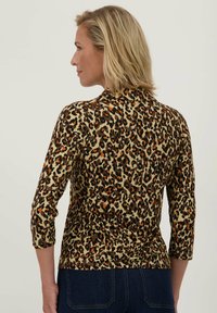 Beige top met luipaardprint, voorzien van driekwart mouwen, een aansluitende pasvorm en een gladde textuur met zwarte, bruine en oranje accenten.