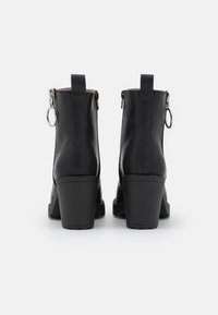 Black leather ankle boots with a chunky heel, side zippers, and a loop accent. Smooth texture with defined stitching and sturdy soles.