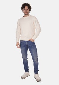 Maglione chiaro in cremoso con polsini e orlo a coste, abbinato a jeans blu e sneakers bianche. Il maglione presenta un colletto rotondo e un tessuto texturizzato.