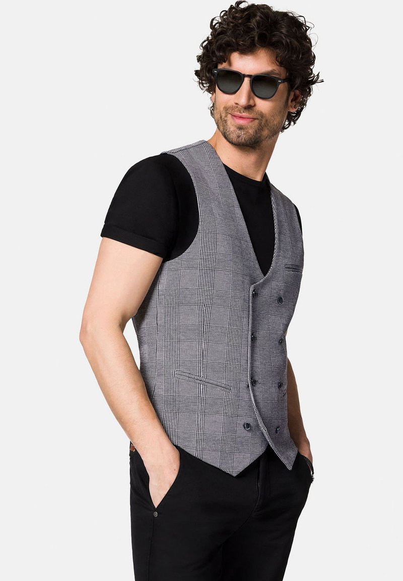 Szary kamizelka w kratę o dopasowanym kroju, z klapami w kształcie notcha, z guzikiem z przodu i kieszeniami na biodrach, noszona na czarnym T-shircie.