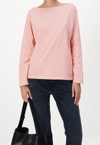 Camisa de manga larga en rosa claro con sutiles rayas, escote barco y corte relajado. Combinada con jeans de mezclilla oscura y un bolso negro.