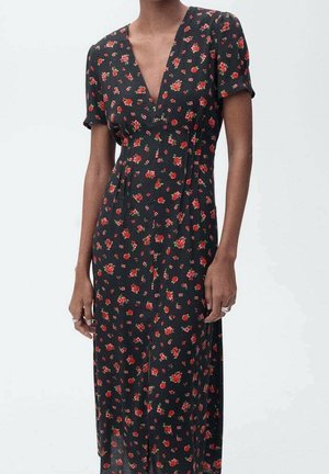 Femme portant une robe midi noire à manches courtes avec un imprimé floral rouge, dotée d'un col en V et d'une taille cintrée.