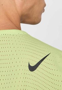 T-shirt de sport vert clair avec une texture perforée et un logo Nike noir sur le côté supérieur gauche. Gros plan de l'arrière de l'encolure.