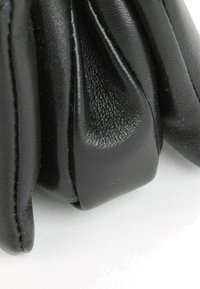Nahaufnahme von schwarzen Lederhandschuhen mit detaillierter Naht und Textur auf den Fingern vor hellem Hintergrund.