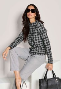 Grijze houndstooth trui met lange mouwen, gecombineerd met grijze op maat gemaakte broek en zilveren hakken. Zwarte leren handtas en oversized zonnebril.
