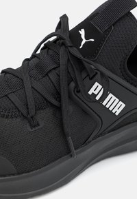 Černá sportovní bota s horním dílem z prodyšné síťoviny, silnou podrážkou, texturovanými tkaničkami a bílým logem Puma na boku pro značkování.