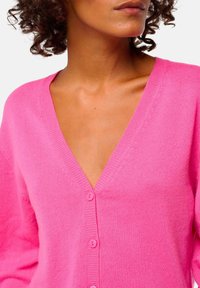 Cardigan rose en V en matière tricotée douce, avec des manches longues et des boutons assortis à l'avant.