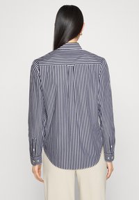 Gestreept shirt met marineblauwe en witte verticale strepen, lange mouwen en een rugstuk met een plooidetail. De stof oogt glad en lichtgewicht.