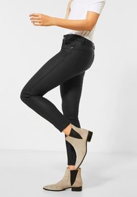 Black skinny jeans with a smooth texture, accented by a traditional five-pocket design, paired with beige ankle boots featuring black side panels.