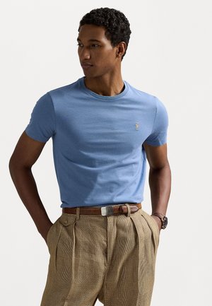 Lichtblauw katoenen t-shirt met een ronde hals, korte mouwen en geborduurd logo op de borst, gecombineerd met geruite bruine geplooide broek.