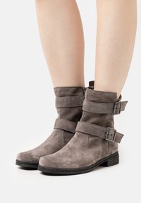 Las botas de tobillo de ante gris presentan dos correas decorativas con hebillas, una puntera redonda, superficie texturizada y un tacón bajo en bloque.