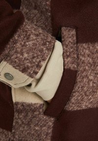 Bruin en beige geruit patroon jas, met een gladde textuur, een drukknoop, en een crème kleurige manchette zichtbaar in de pocket.