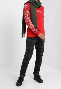 Punainen joulupaita valkoisin kuvioin ja vihreä huivi, yhdistetty mustiin ja vihreisiin ruudullisiin housuihin sekä mustiin lenkkareihin.