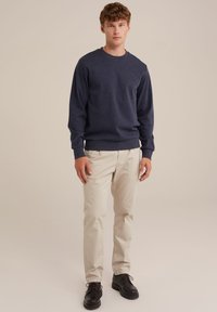 Marinblå sweatshirt med ribbade ärmmuddar, rund hals och en strukturerad tygkvalitet. Kombinerad med ljusbeiga byxor och svarta snörskor.