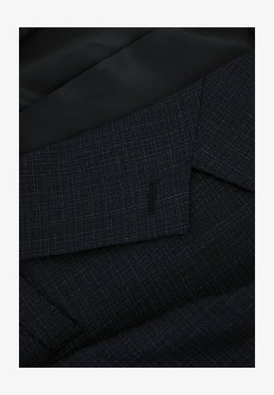 Mörk skräddarsydd kostymtyg med ett subtilt rutig mönster, med texturerade marinblå och svarta lager, och en slät innerfoder. Accenterad med en liten svart lås.