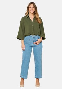 Green oversized shirt with a button-up design and rolled sleeves, paired with light blue wide-leg jeans and beige heels.
