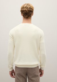 Cremefarbener Strickpullover mit gerippter Textur, runder Kerbkragen und langen Ärmeln. Der Saum und die Manschetten sind leicht tailliert, was die Form betont.