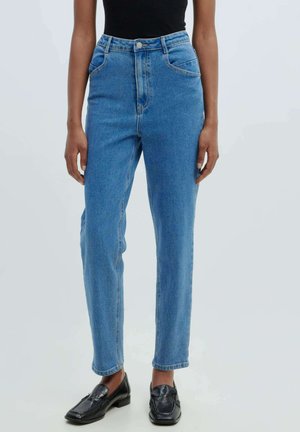 Hoog-was blauwe denim jeans met een rechte pijp, vijf-pocket ontwerp en zichtbare stiksels. Gecombineerd met zwarte instapschoenen.