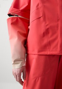 Coral waterproof jacket with a textured finish and contrasting light-colored sleeves. Features a hidden zipper and patch pocket detail.