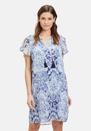 Kurzärmeliges, blau gemustertes Kleid mit V-Ausschnitt und Quastenakzenten. Es weist ein florales Design in hellen und dunklen Blautönen auf.