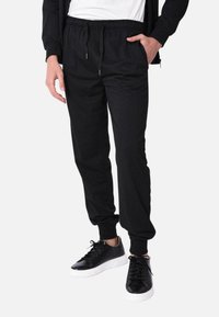 Pantaloni da jogging neri con vita elastica e cordino, dotati di tasche laterali e polsini affusolati. Indossati con sneaker nere.