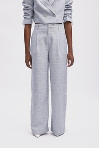 Pantalon large taille haute de couleur gris clair, en tissu texturé, présentant des plis nets. Des chaussures à bout pointu viennent compléter le look.