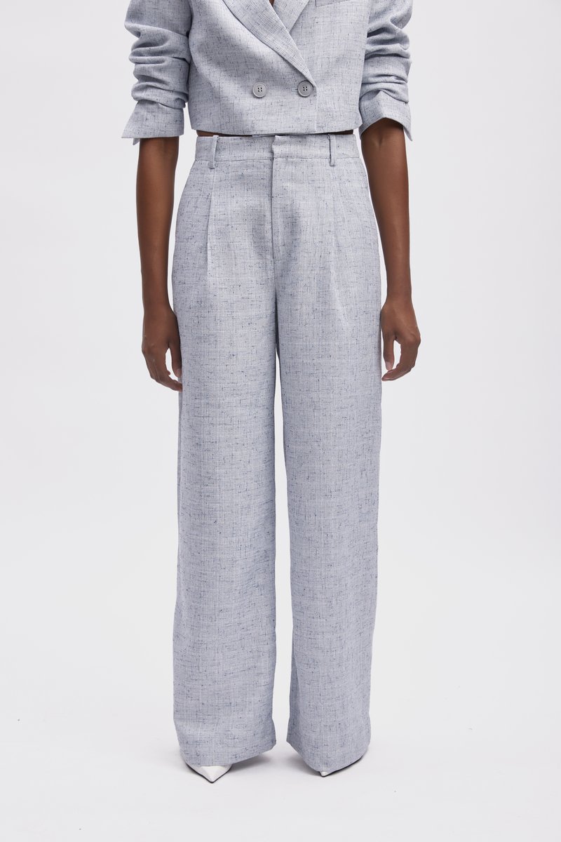 Pantalon large taille haute de couleur gris clair, en tissu texturé, présentant des plis nets. Des chaussures à bout pointu viennent compléter le look.