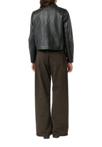 Schwarze, kurz geschnittene Lederjacke mit langen Ärmeln, glatter Textur und minimalistischem Design. Kombiniert mit braunen, weit geschnittenen Hosen mit Taschen.