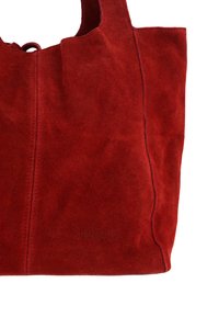 Rød suede tote taske med blød tekstur, der har stikninger og prægning af "Venezia" branding på siden. Åben topdesign.