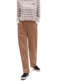 Jasnobrązowe, szerokie spodnie z bocznymi kieszeniami, z teksturowanej tkaniny, zestawione z białą koszulą w paski z długim rękawem i czarnymi trampkami.