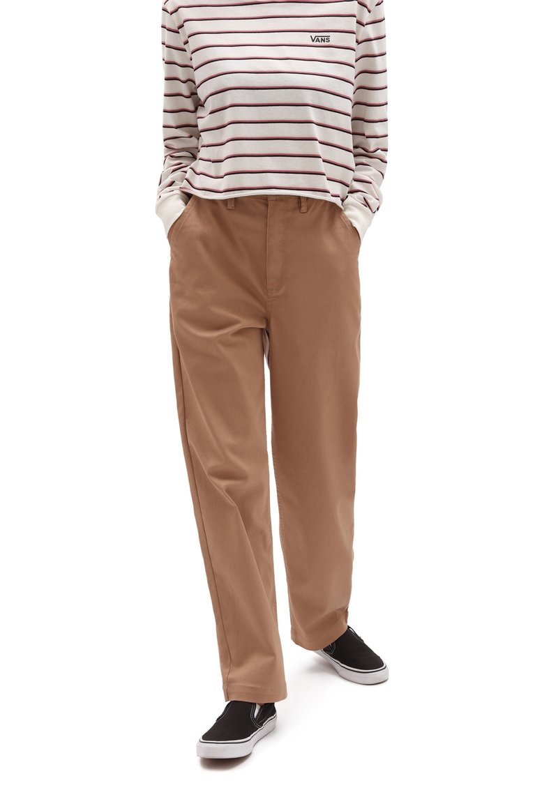 Jasnobrązowe, szerokie spodnie z bocznymi kieszeniami, z teksturowanej tkaniny, zestawione z białą koszulą w paski z długim rękawem i czarnymi trampkami.