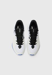 Baskets blanches avec des lacets et des accents noirs, en matériaux mesh et synthétiques, à bout rond, avec des détails bleus sur la semelle.