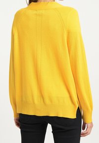 Žlutý pletený svetr s volným střihem, žebrovaným lemem a bočními rozparky. Má kulatý výstřih a raglánové rukávy, vyrobený z měkké látky.