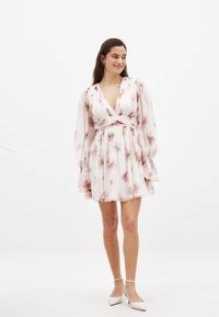 Mini obleka s cvetličnim vzorcem v svetlo rožnati barvi, z globokim V-izrezom, dolgimi nabranimi rokavi in pasom. Narejena iz lahkega, tekočega materiala.