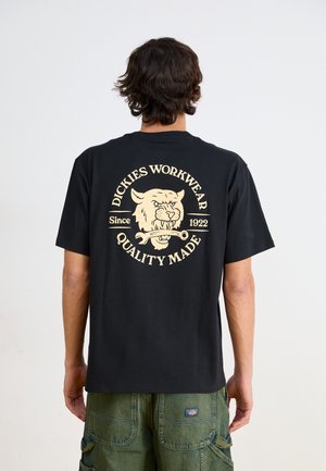 Black cotton t-shirt featuring a cream graphic on the back with a lion's head, including text "DICKIES WORKWEAR Since 1922 QUALITY MADE."
