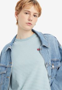 Dryžuotas šviesiai mėlynas marškinėliai su Levi's logotipu, dėvimi po išblukusiu džinsiniu švarku. Turi apvalų kaklą ir trumpas rankoves.