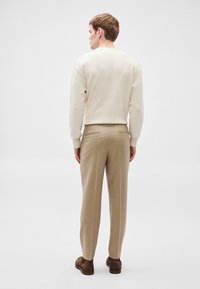 Μπεζ ριγωτό πουλόβερ, σε κρεμ απόχρωση, συνδυασμένο με ανοιχτό μπεζ παντελόνι και καφέ παπούτσια, από πίσω όψη. Απλός σχεδιασμός και κοπή.