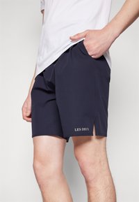 Marineblå svømmebukser lavet af letvægtsstof, med sideslids, elastisk talje og "LES DEUX" broderet i bunden.