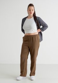 Brown striped pants with an elastic waistband paired with a white cropped tank top and a sheer gray long-sleeve overlay. White sneakers.