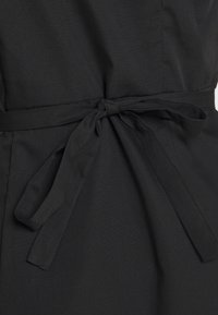 Vestido de tela negra con detalle de cintura atada, textura suave y diseño simple con silueta recta. Sin patrones o acentos destacados.