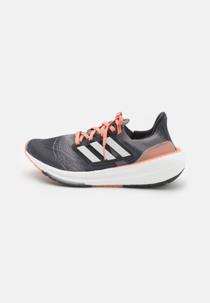 Schwarzer und grauer Sportschuh mit pinken Schnürsenkeln, drei weißen Streifen, strukturiertem Obermaterial und einer dicken weißen Sohle mit schwarzen Akzenten.